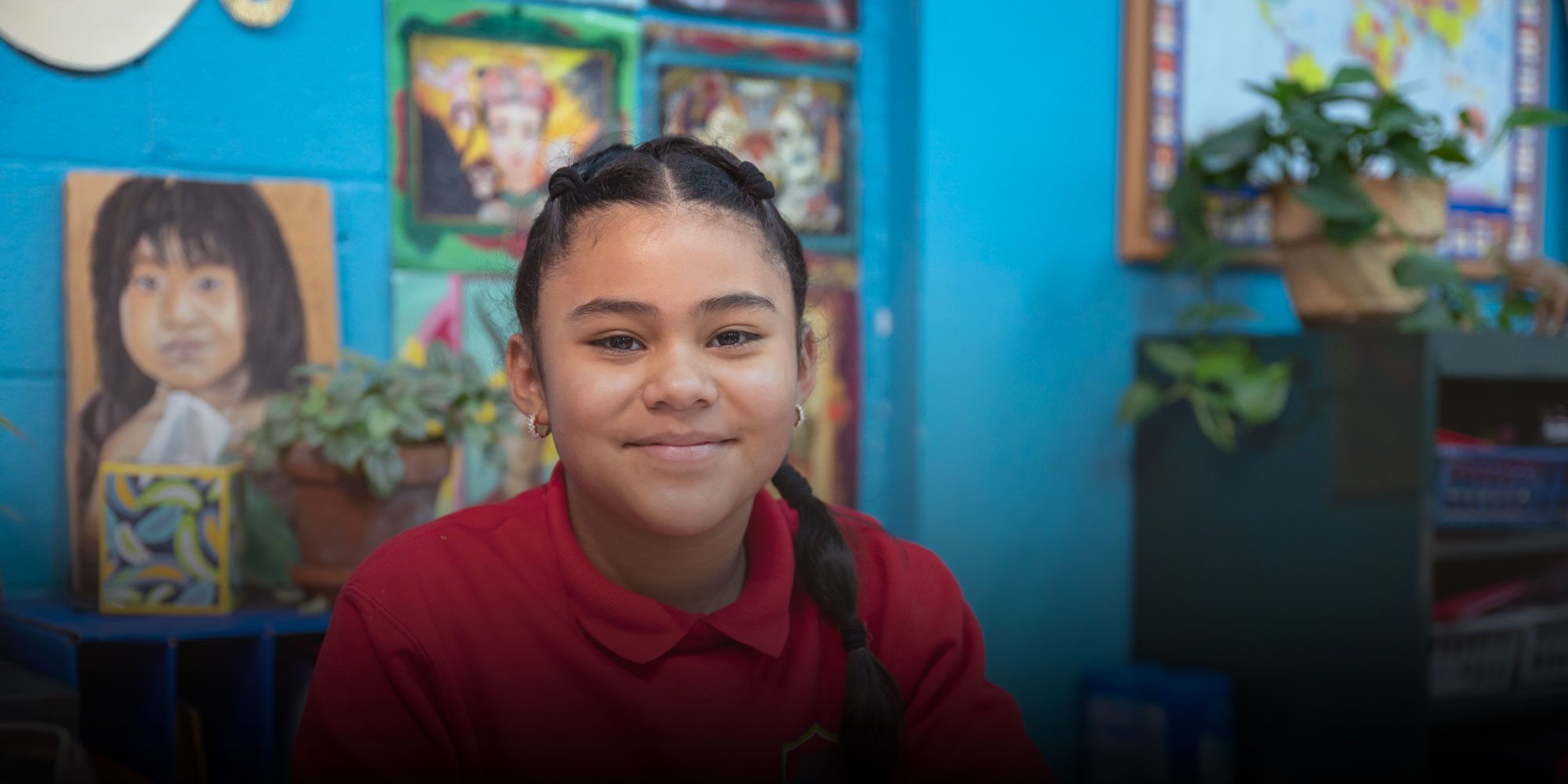 Smiling student in a red uniform in front of classroom artwork.