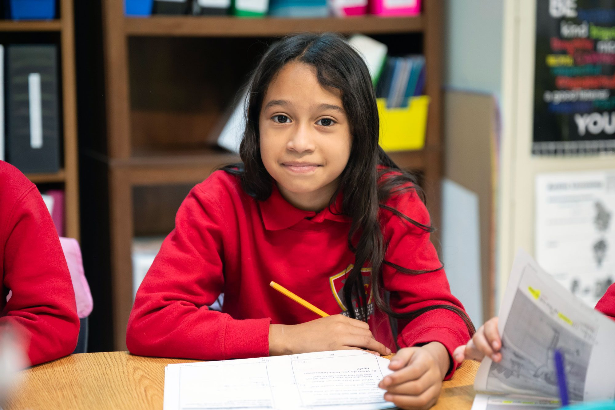 Student in a red uniform working on a worksheet with a pencil.